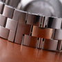 Close-up of stainless steel watch bracelet with polished and brushed link segments on brown leather surface.