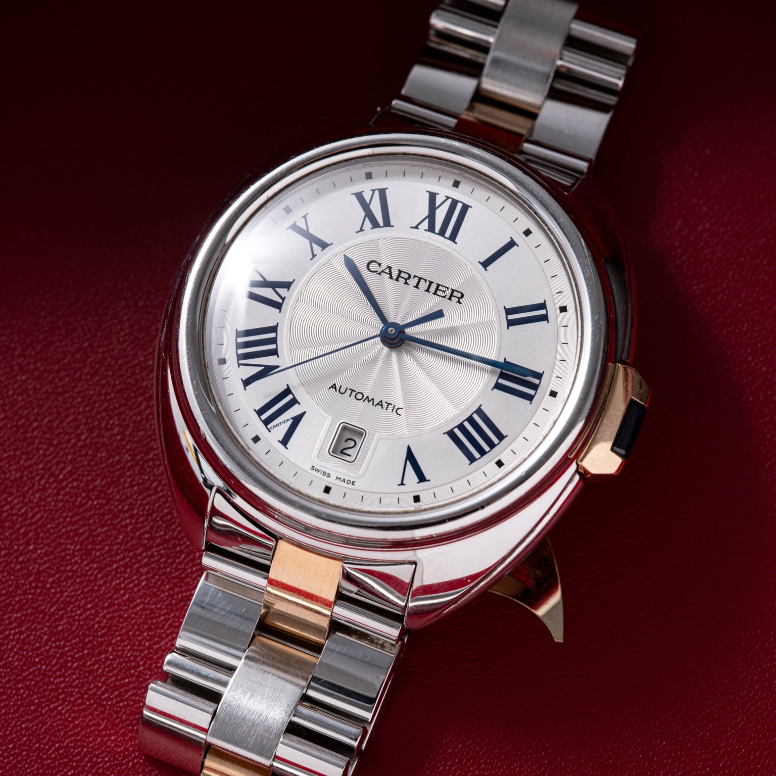 Cartier automatic watch with white dial, Roman numerals, date window, and two-tone metal bracelet.