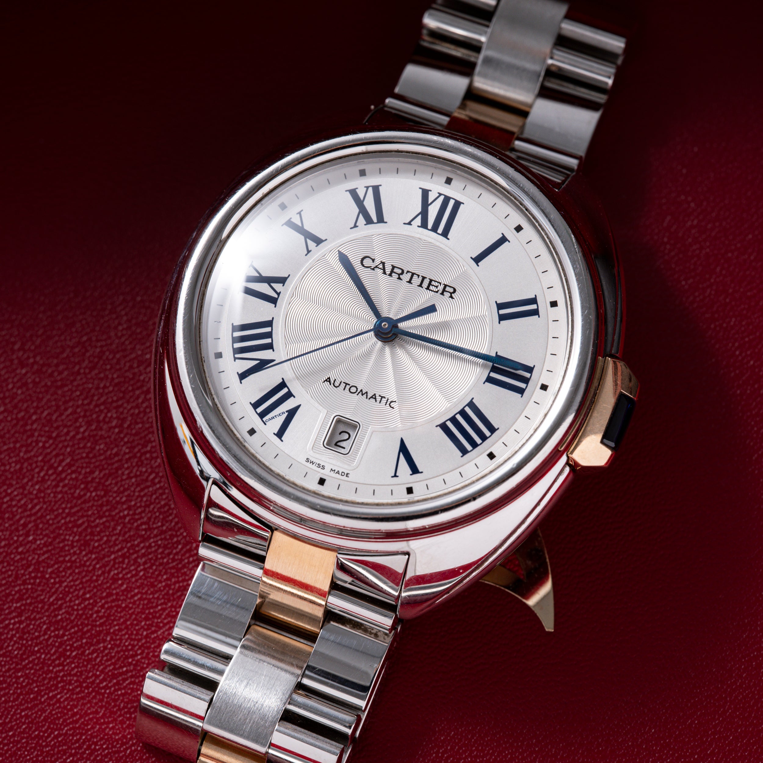 Cartier automatic watch with white dial, Roman numerals, date window, and two-tone metal bracelet.