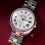 Cartier automatic watch with white dial, Roman numerals, date window, and two-tone metal bracelet.