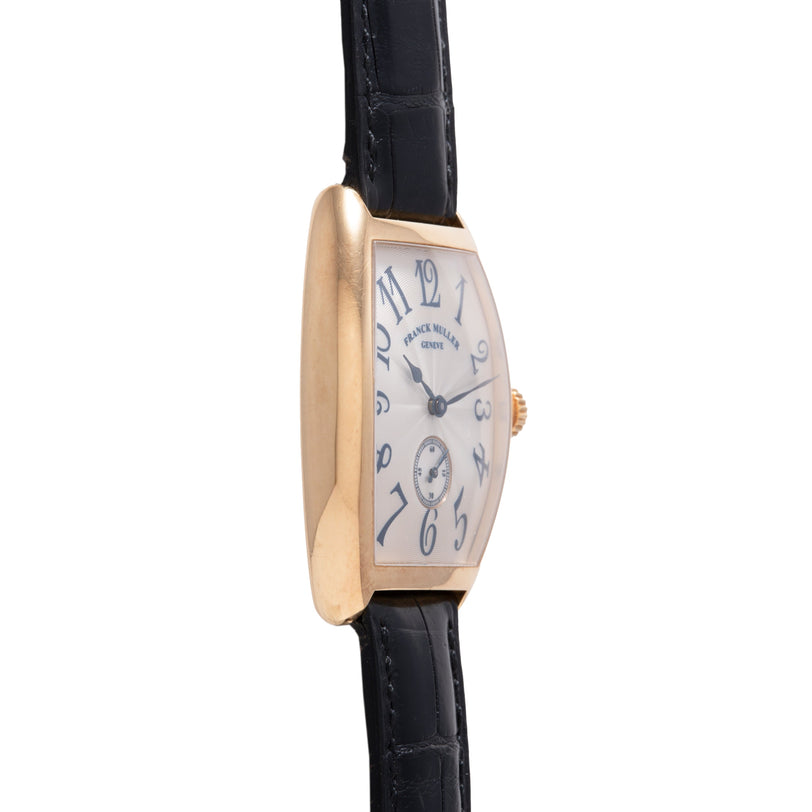Gold-tone curved rectangular watch with cream dial, blue numerals, and black leather strap.