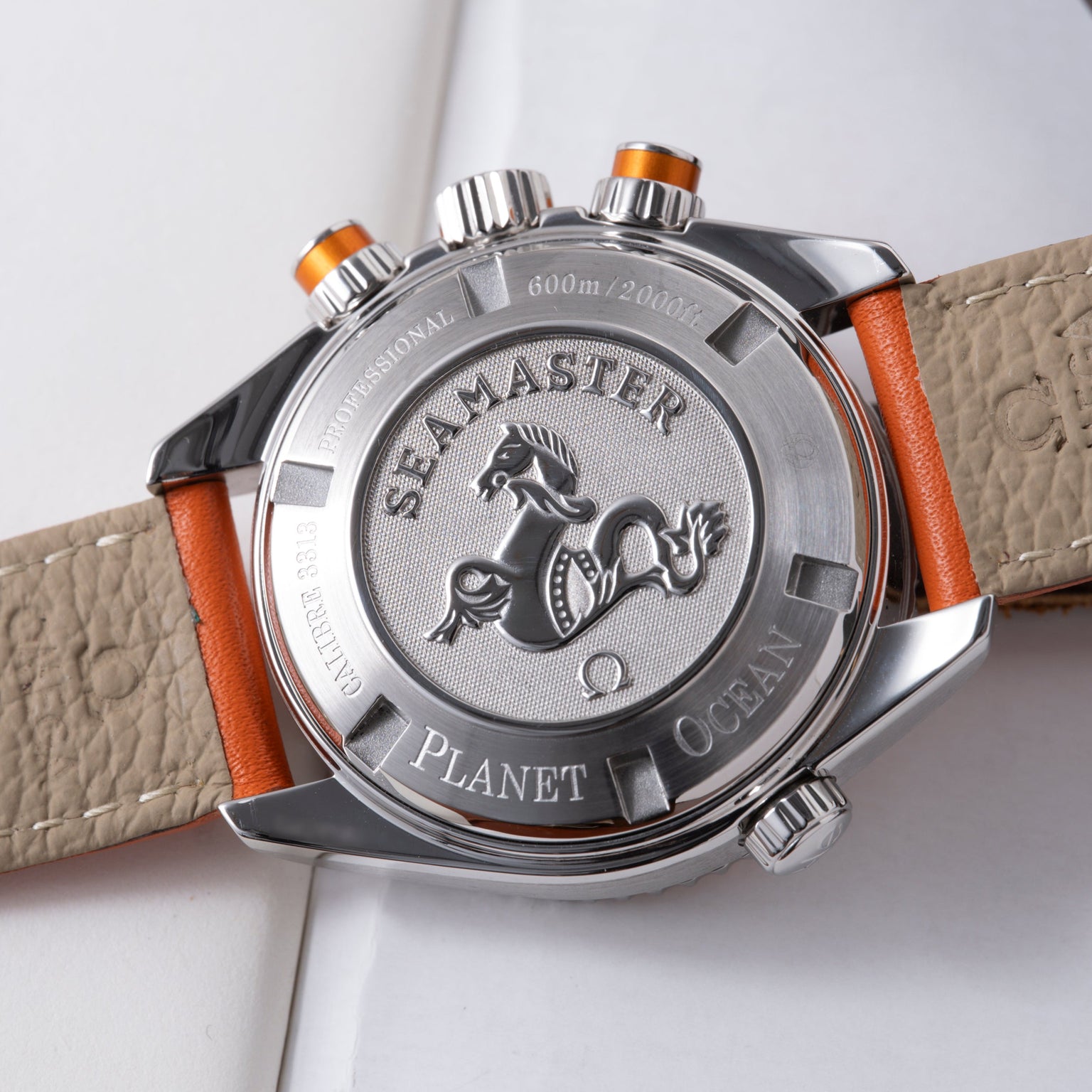 Stainless steel chronograph watch with orange and beige leather strap, showing caseback with seahorse emblem and 600m depth r