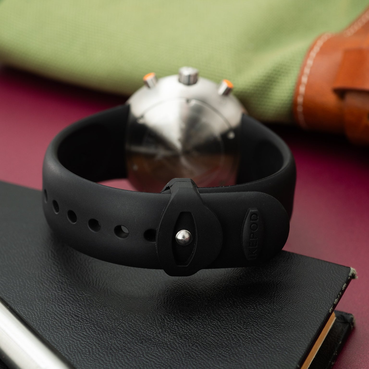 Black rubber strap chronograph watch with white dial and orange pushers, displayed on black leather.