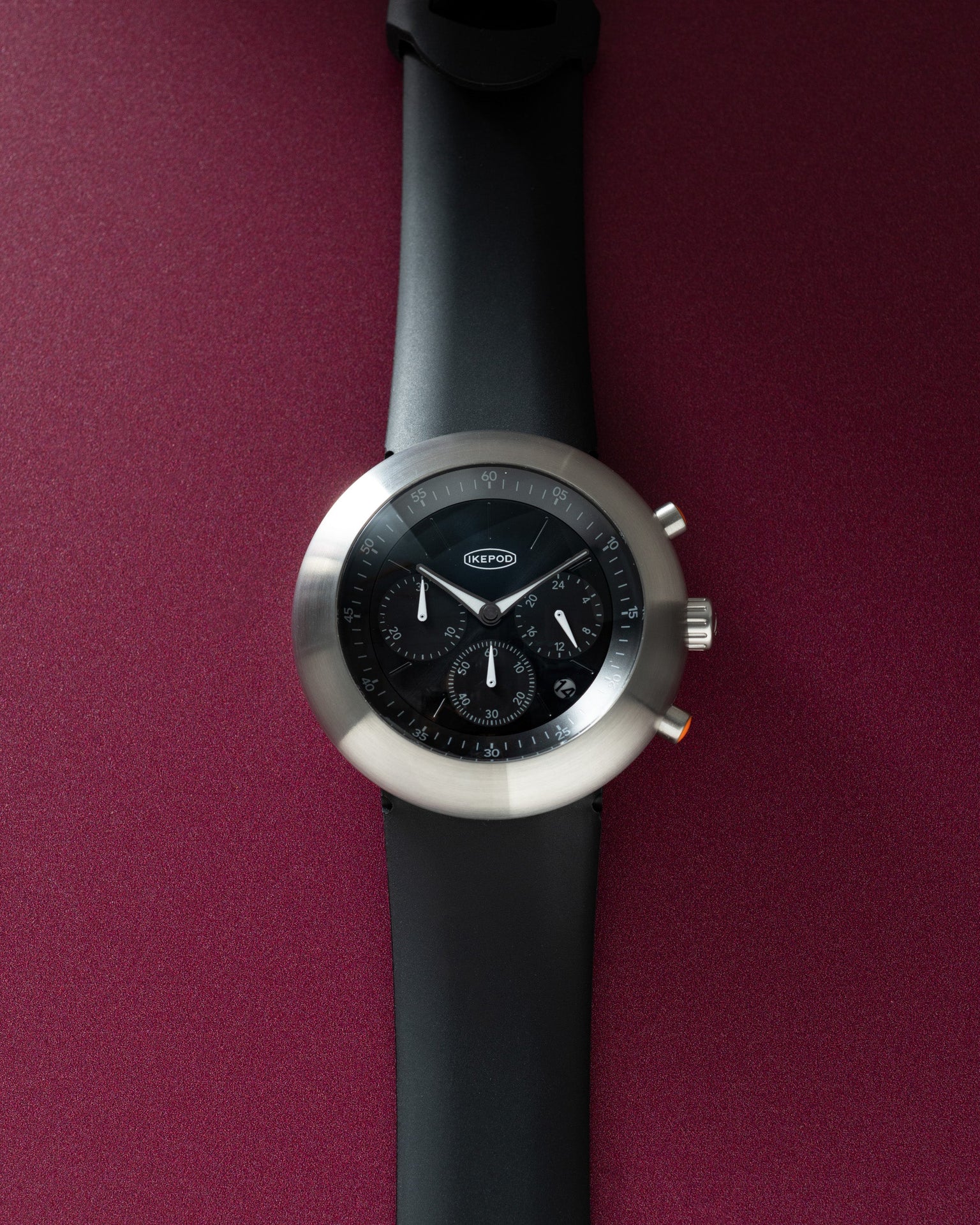 Black chronograph watch with silver round case, black dial with subdials, and black rubber strap.
