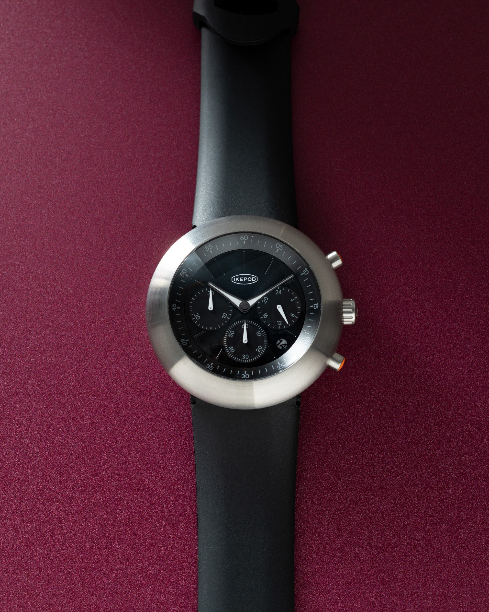 Black chronograph watch with silver round case, black dial with subdials, and black rubber strap.