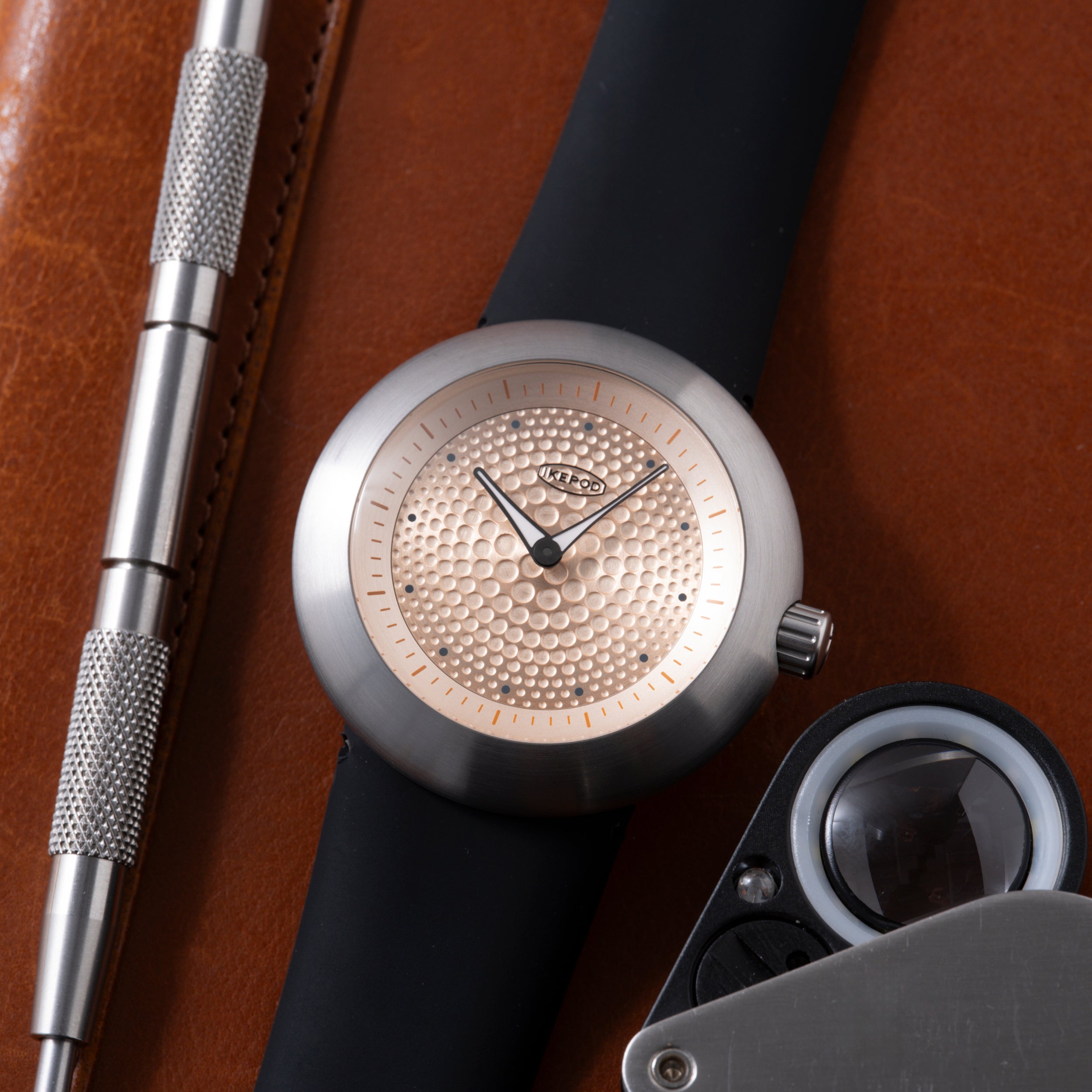Silver watch with champagne dial featuring small dots pattern, black strap, and black hands on brown leather background.