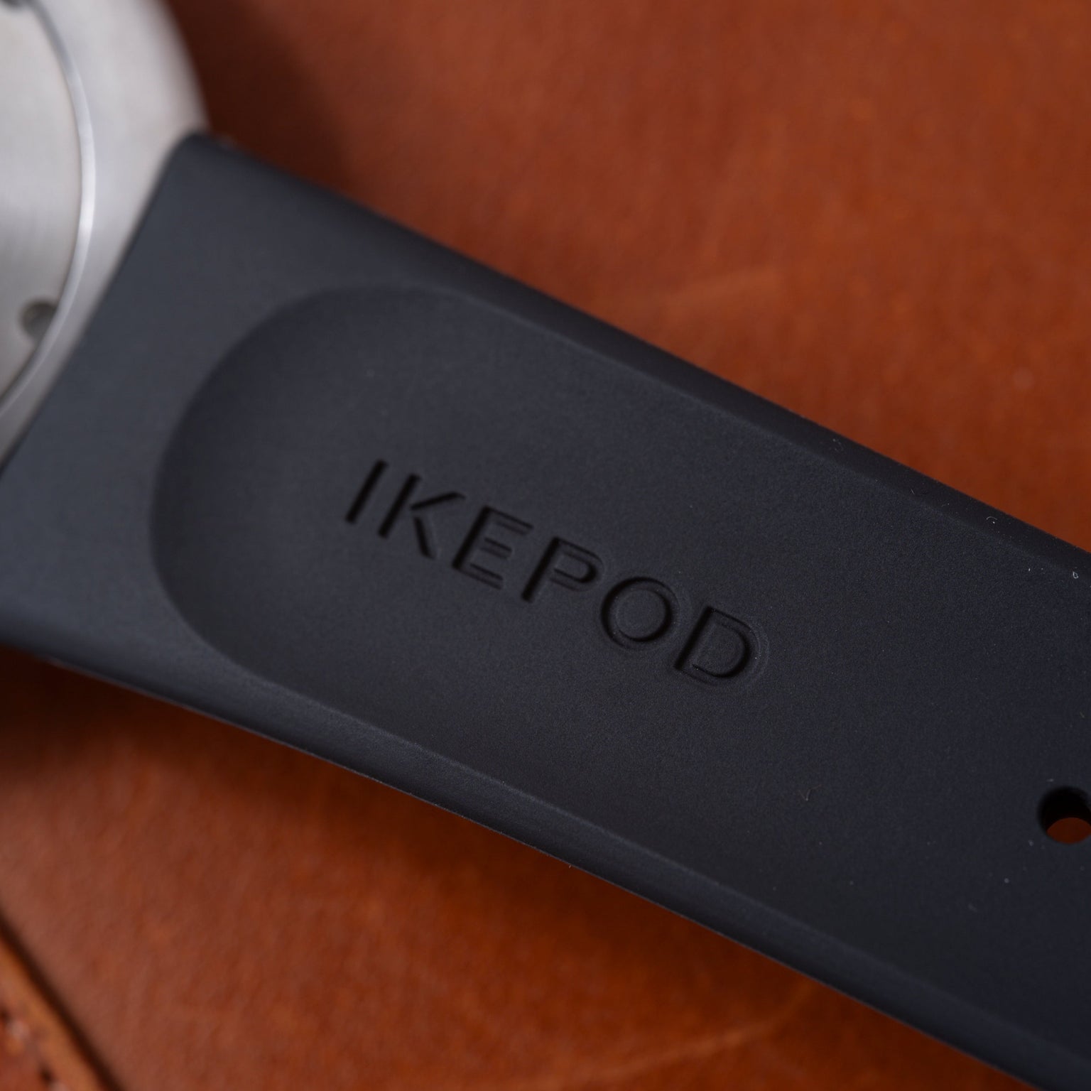 Dark blue Ikepod Duopod device with white earpiece visible, placed on cognac-colored leather surface.