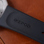 Dark blue Ikepod Duopod device with white earpiece visible, placed on cognac-colored leather surface.