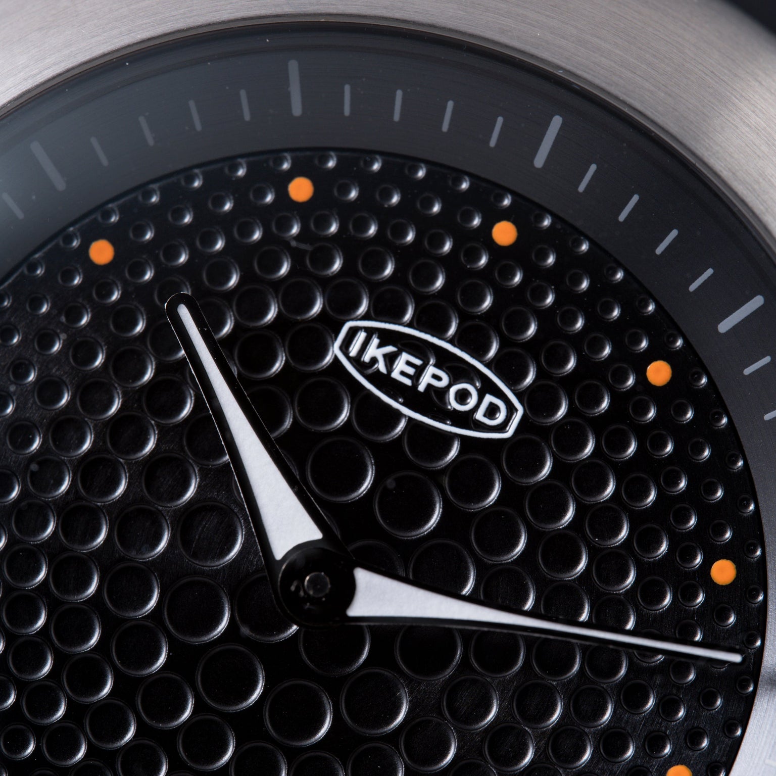 Black watch dial with textured dot pattern, white hands, orange accent markers, and Ikepod branding.