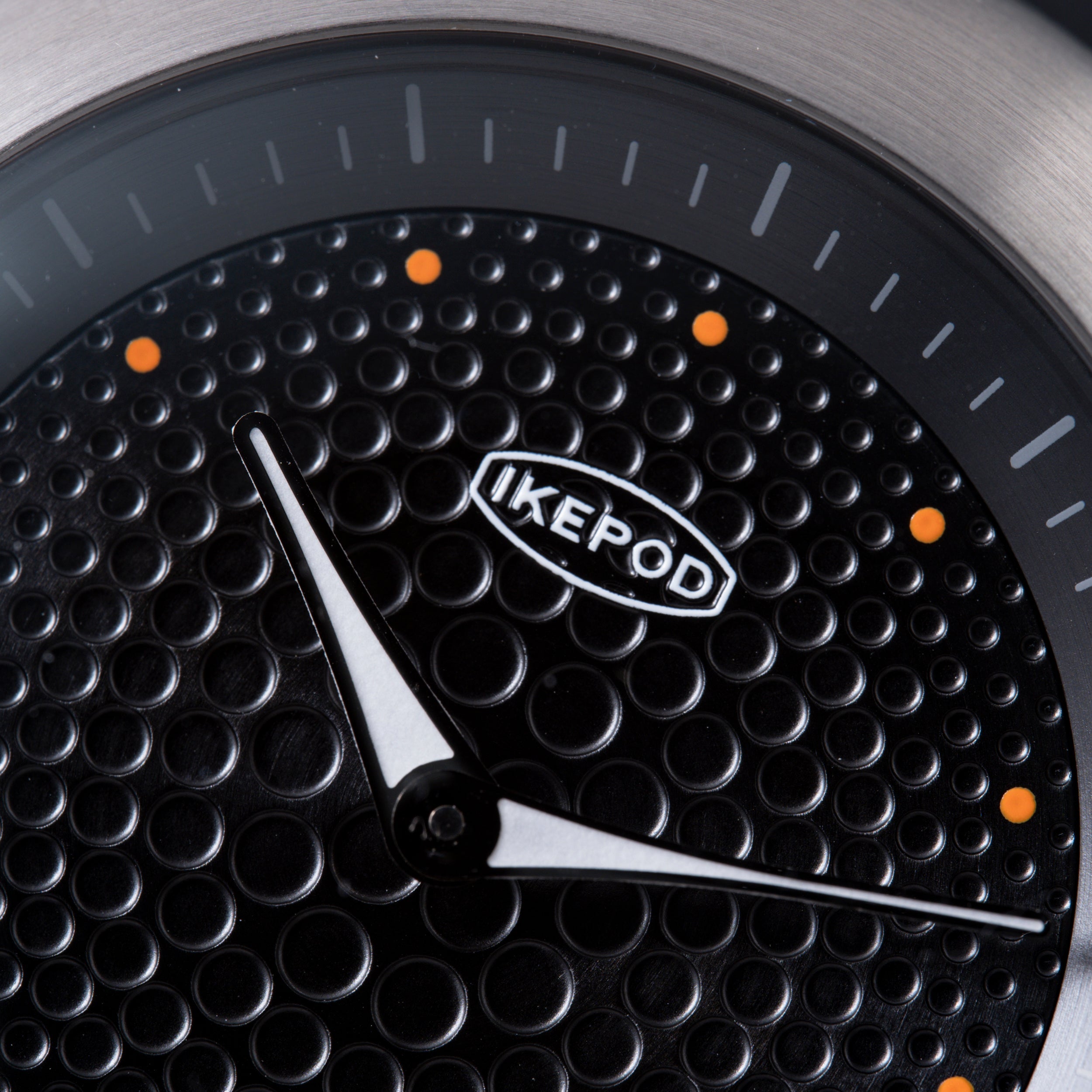 Black watch dial with textured dot pattern, white hands, orange accent markers, and Ikepod branding.