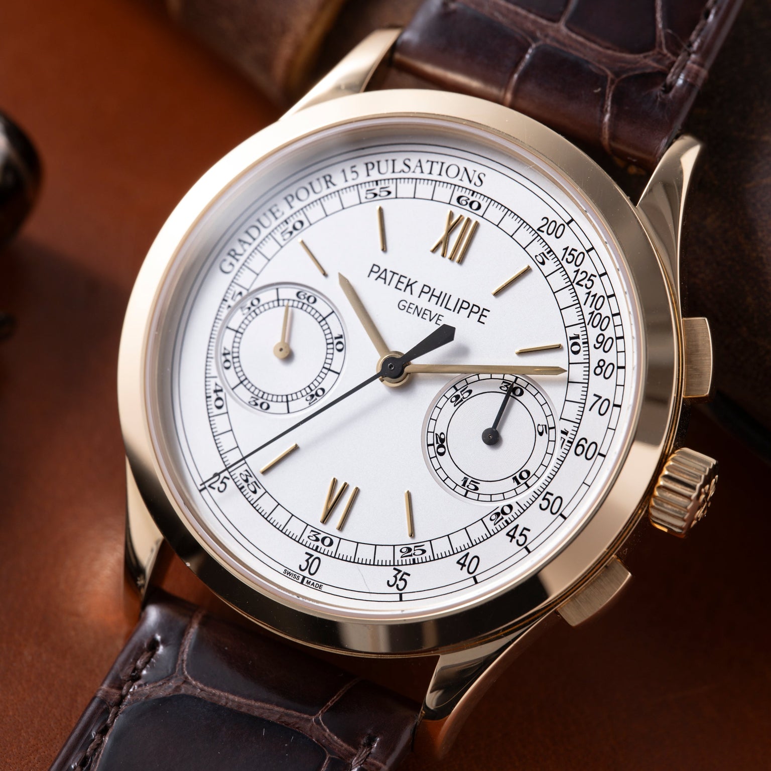 Patek Philippe chronograph watch with white dial, Roman numerals, subdials, and brown leather strap.