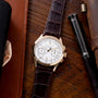 Patek Philippe chronograph with white dial, two subdials, and dark crocodile leather strap on wooden surface.