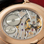 Rose gold watch caseback displaying exposed mechanical movement with gears, jewels, and engraved text.