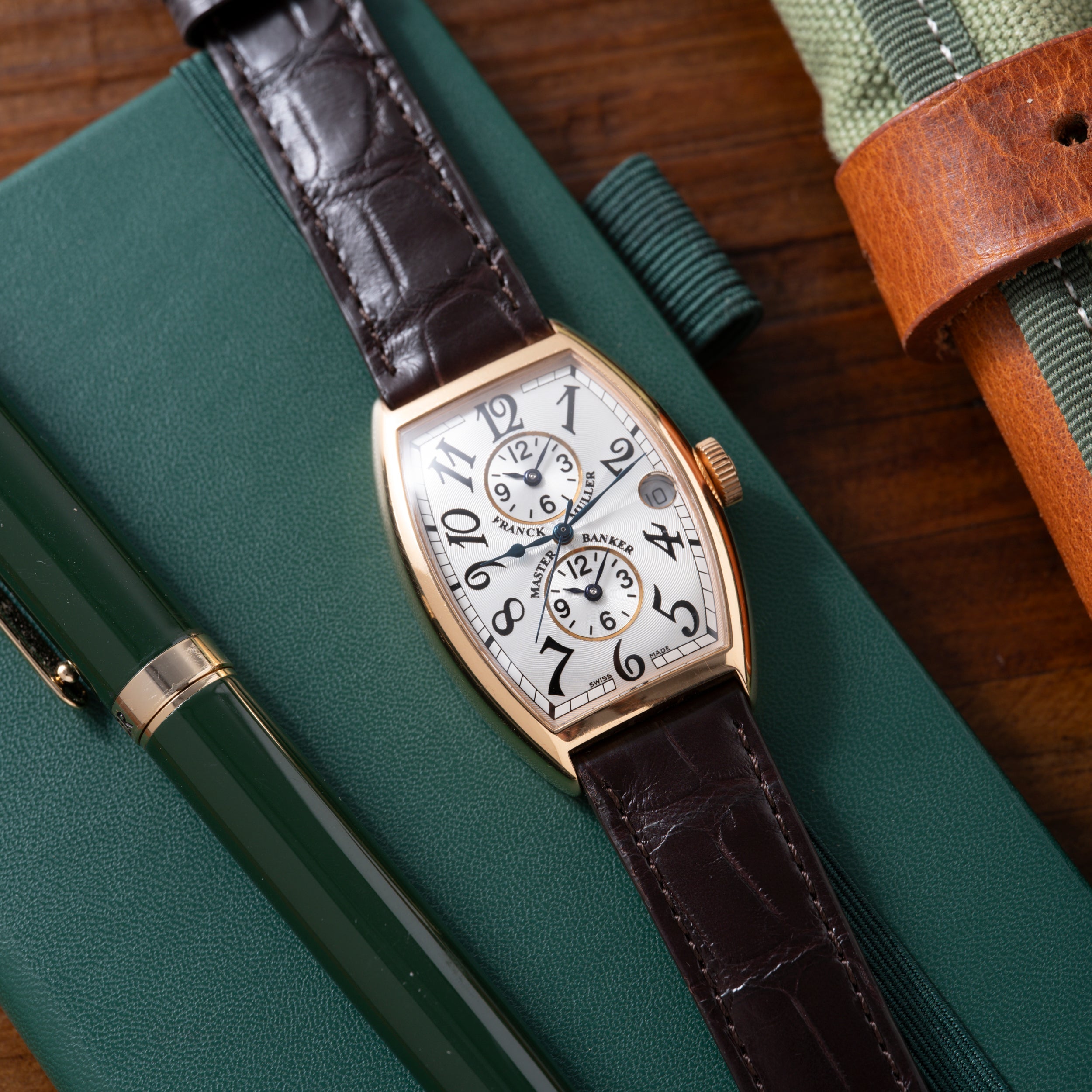 Rose gold tonneau watch with white dial, dual subdials, black crocodile strap on green leather surface.