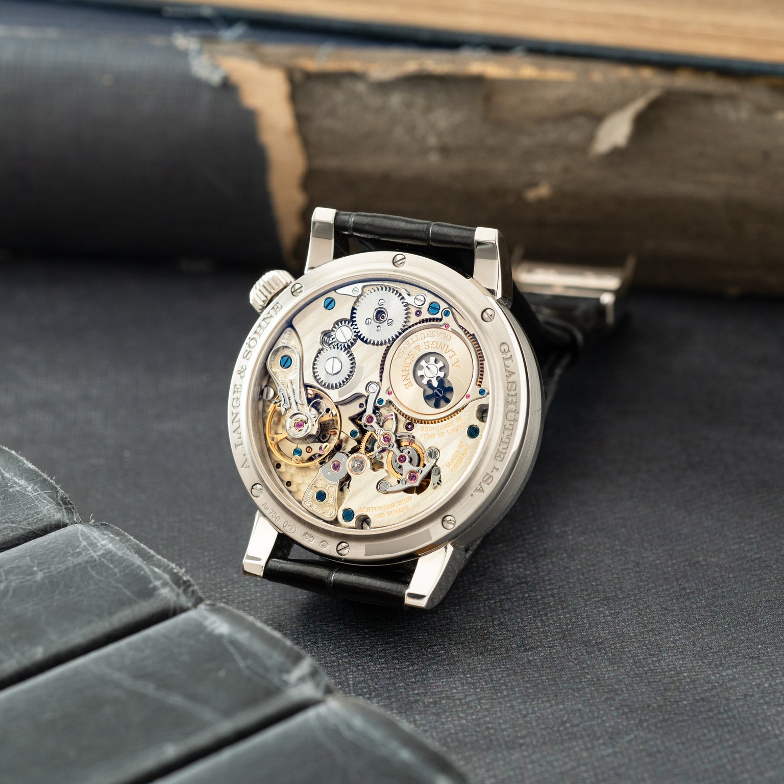 Silver watch with black leather strap displaying exposed mechanical movement with gears, jewels, and balance wheel visible th