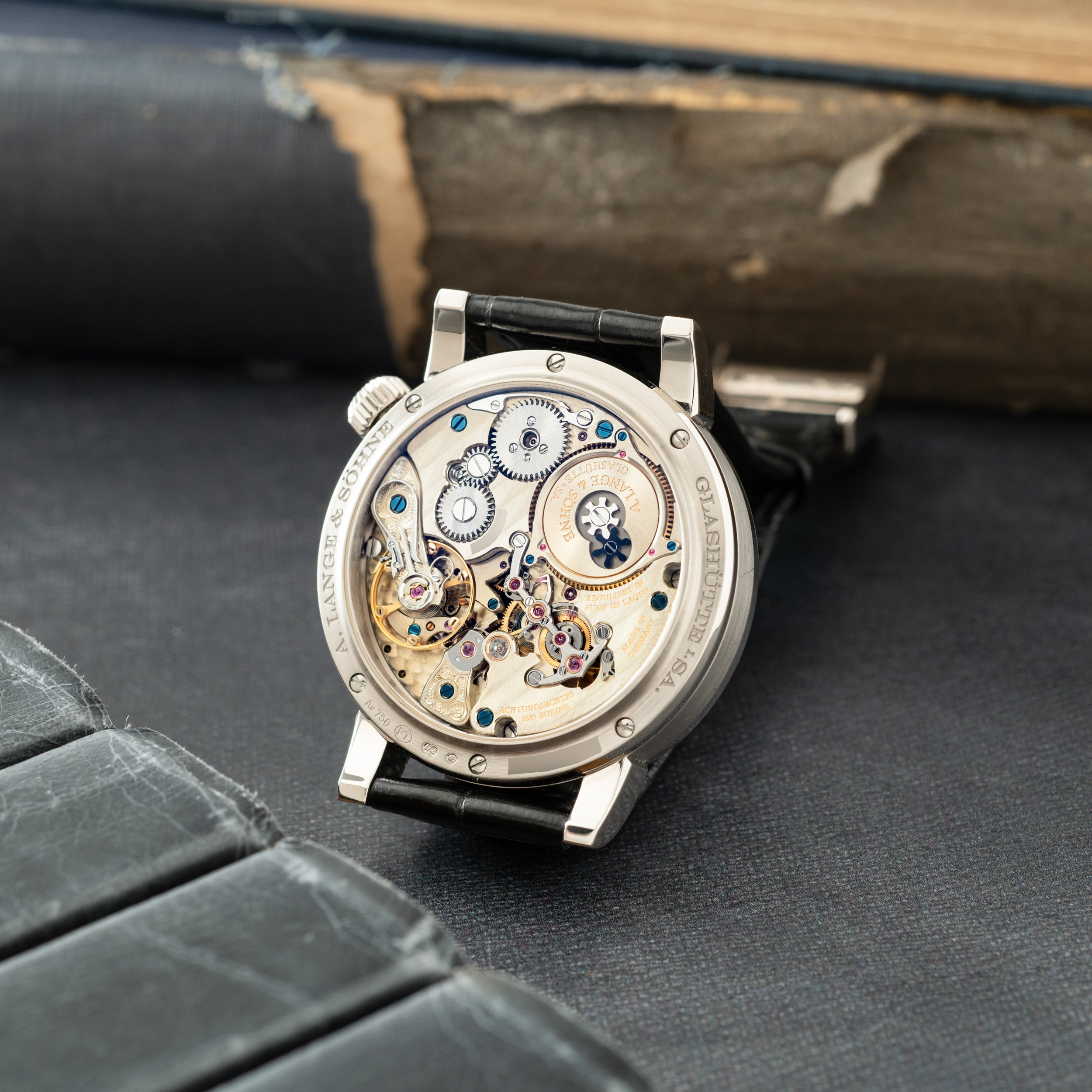 Silver watch with black leather strap displaying exposed mechanical movement with gears, jewels, and balance wheel visible th