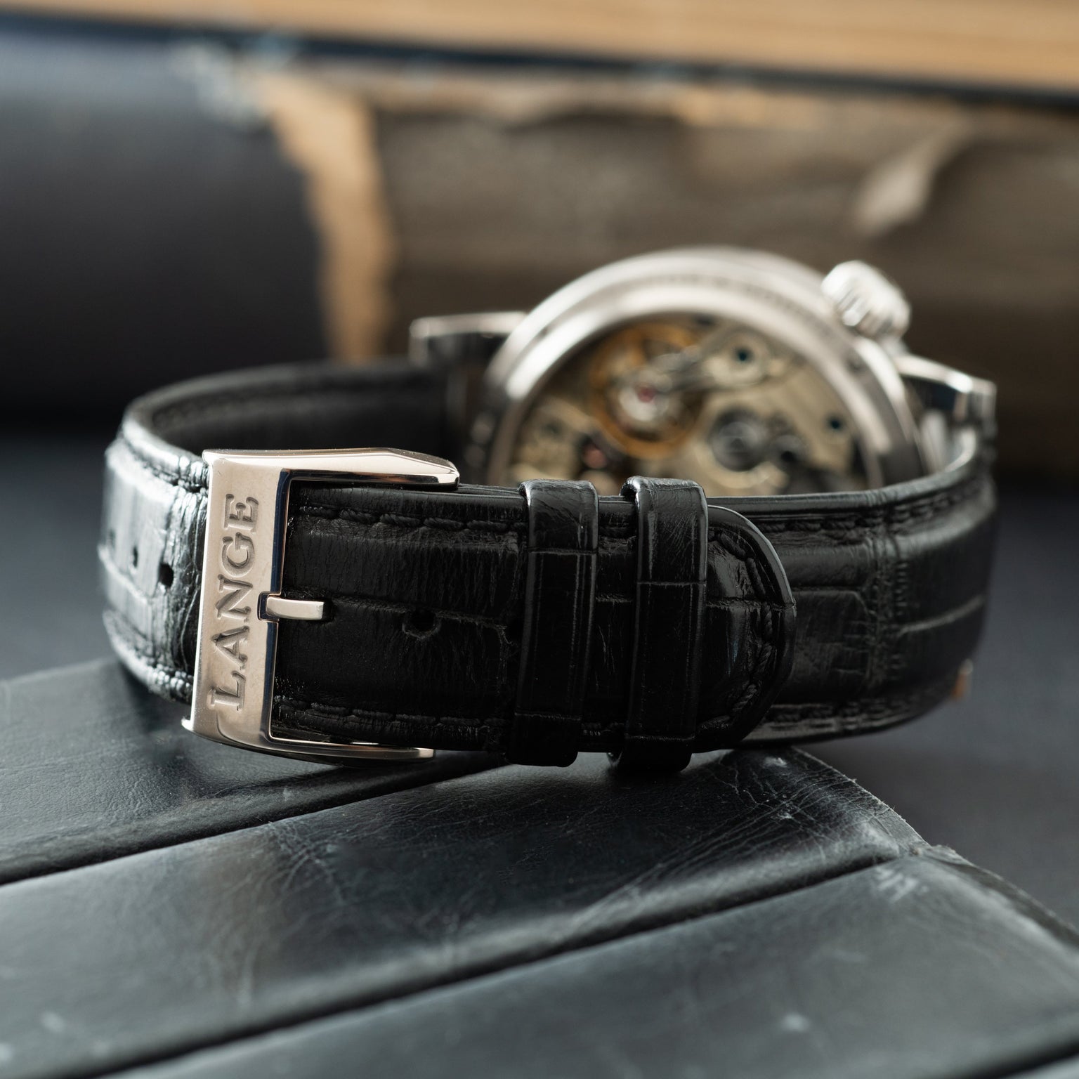 Silver-cased watch with exposed movement visible through display caseback, black leather strap with A. Lange & Söhne buckle.