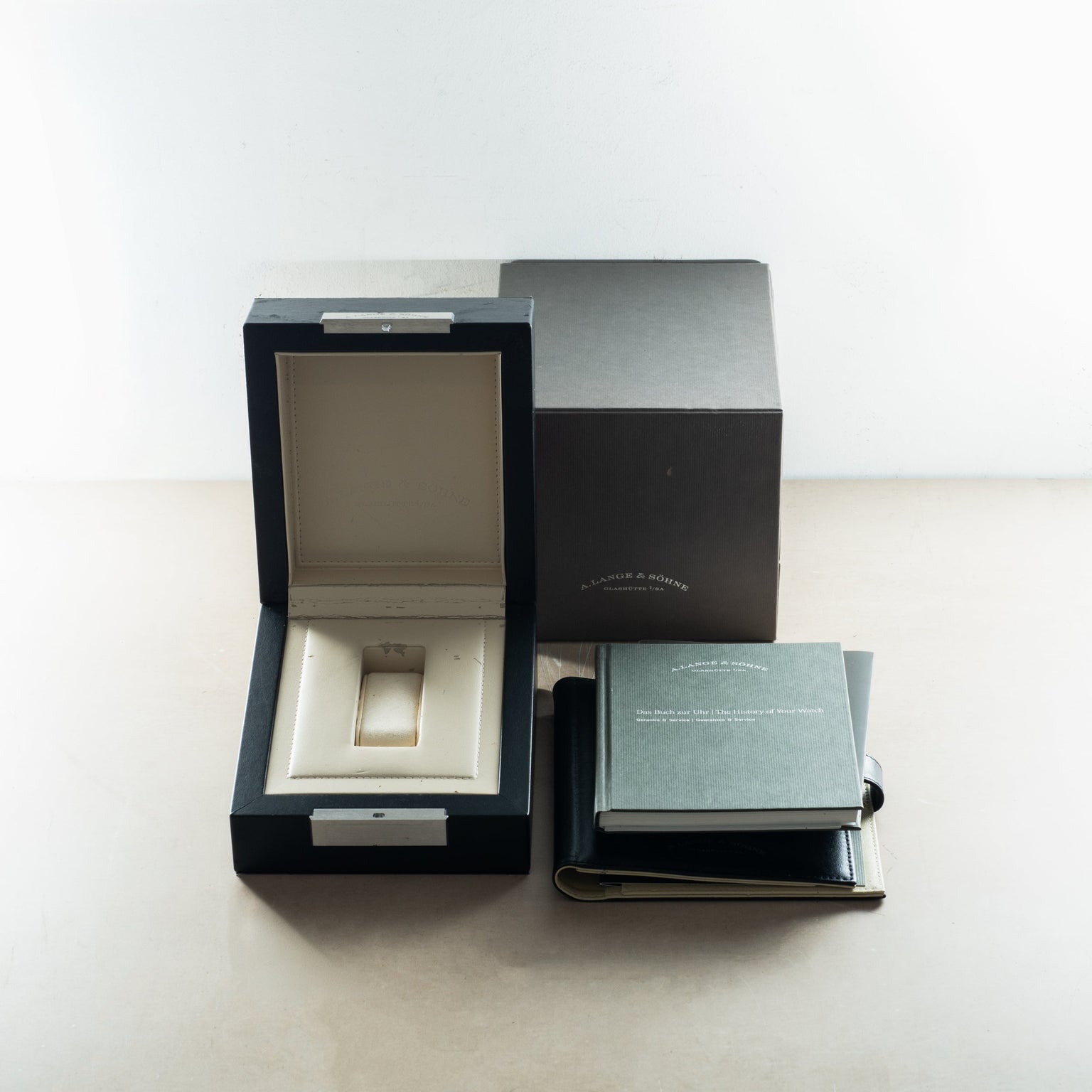 A. Lange & Söhne watch box set with open black presentation case, cream interior cushion, outer box, and documentation bookle