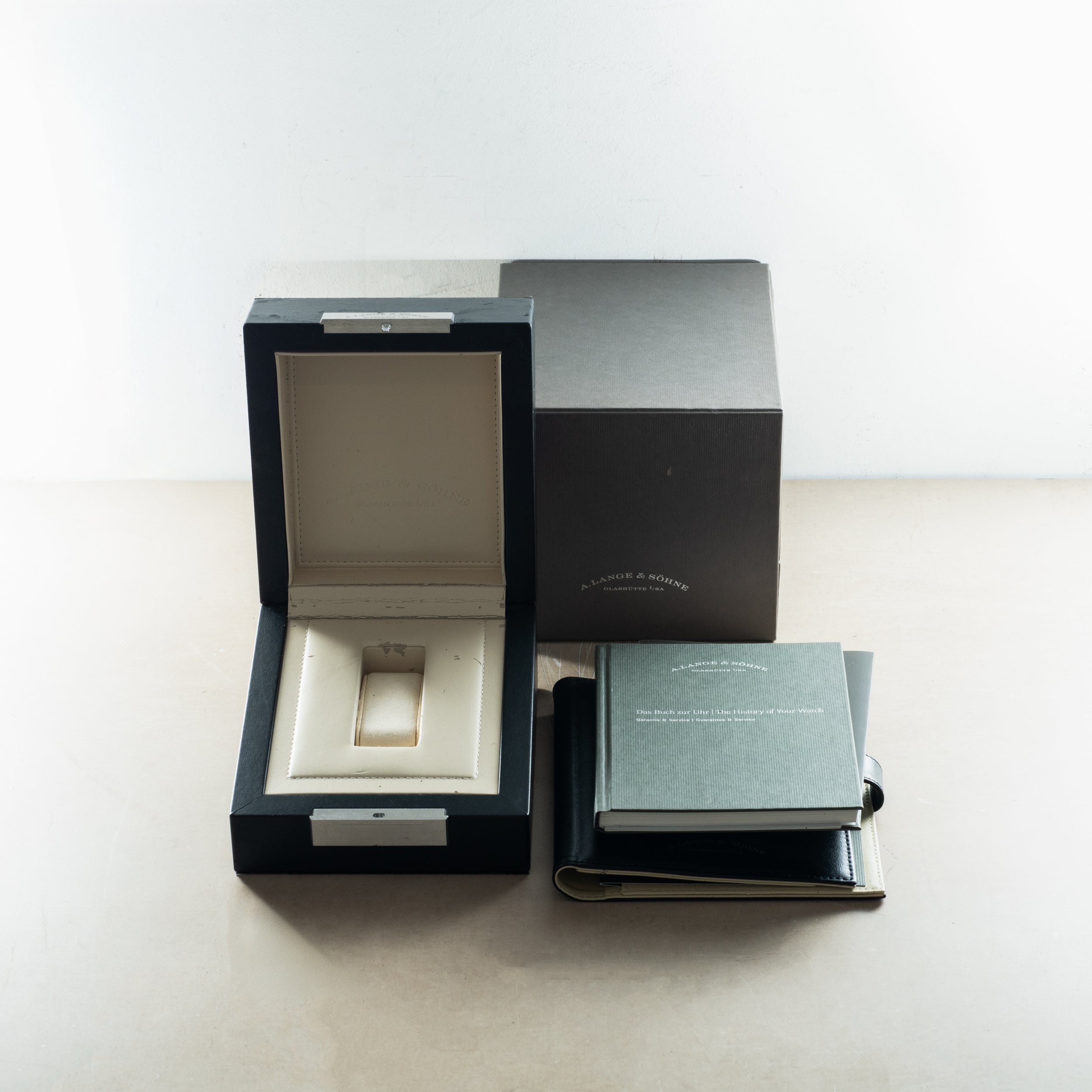 A. Lange & Söhne watch box set with open black presentation case, cream interior cushion, outer box, and documentation bookle