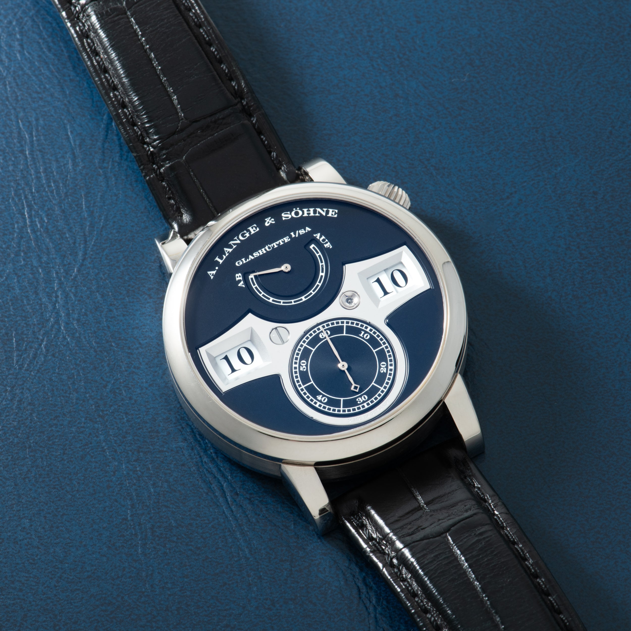 Silver-cased watch with dark blue dial, white digit displays showing "10", and small subdial, paired with black crocodile lea