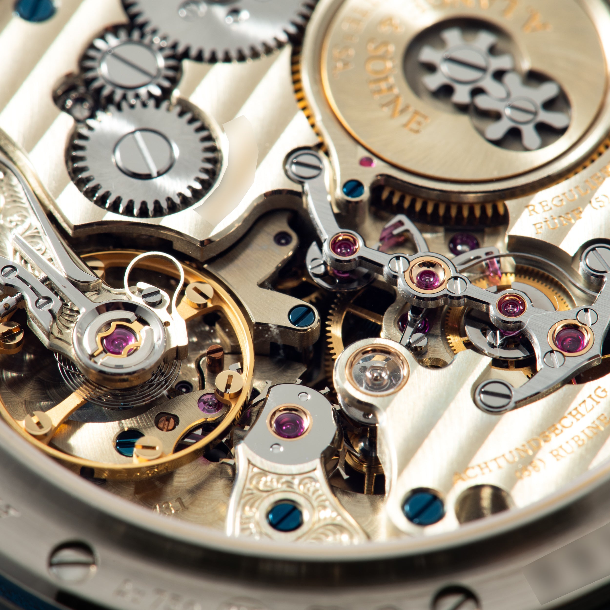 Close-up of watch movement showing polished steel and gold gears, escapement, and jeweled bearings with engraved text.
