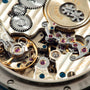 Close-up of watch movement showing polished steel and gold gears, escapement, and jeweled bearings with engraved text.