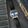 A. Lange & Söhne Zeitwerk watch with blue dial, white numerals, black leather strap on dark fabric surface.