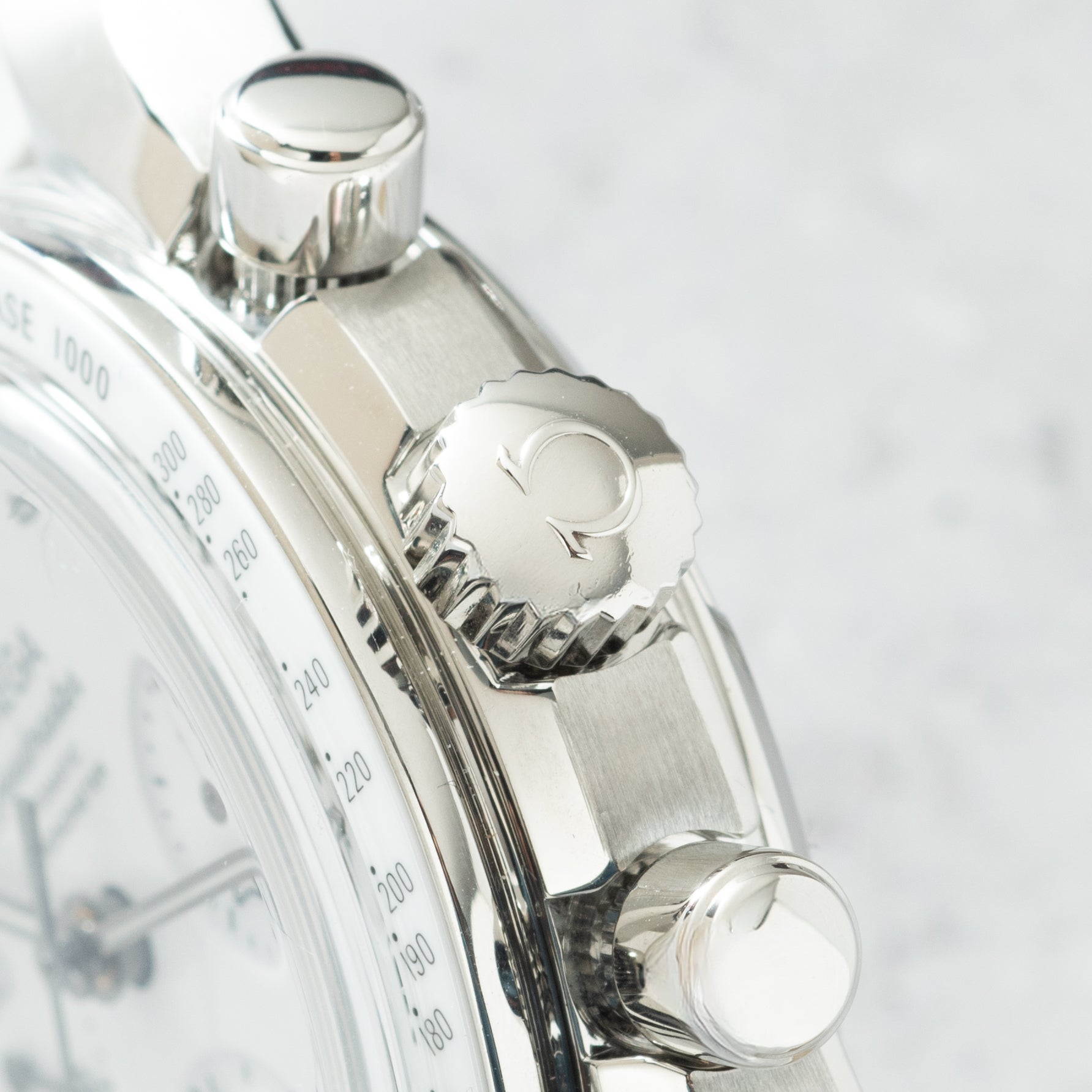Stainless steel chronograph watch with three polished pushers and tachymeter bezel dial, shown in close-up detail.