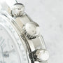 Stainless steel chronograph watch with three polished pushers and tachymeter bezel dial, shown in close-up detail.