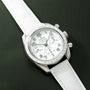 Omega Speedmaster chronograph with white dial, tachymetre bezel, and white leather strap on green background.