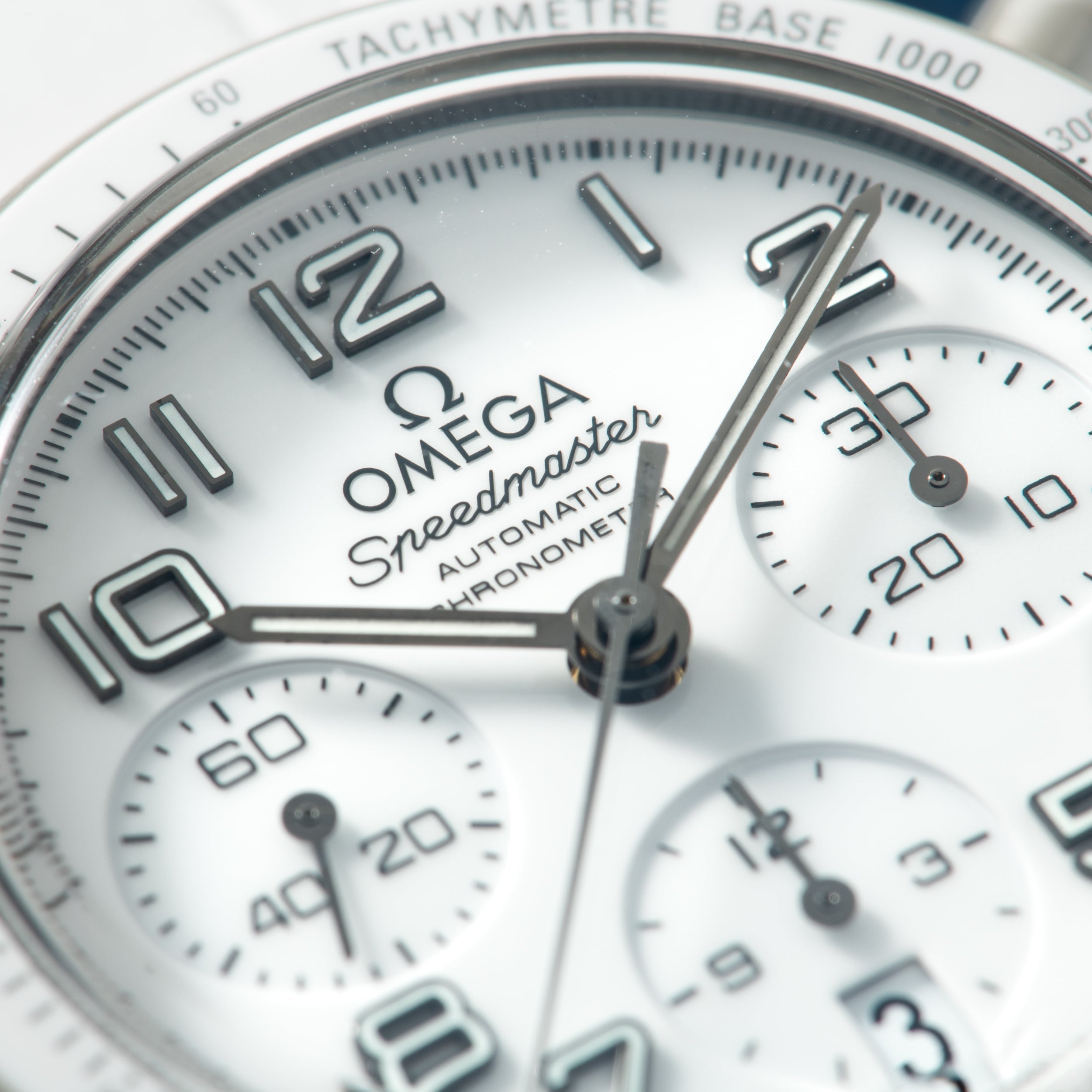Omega Speedmaster chronograph watch face with white dial, tachymeter bezel, and multiple subdials.