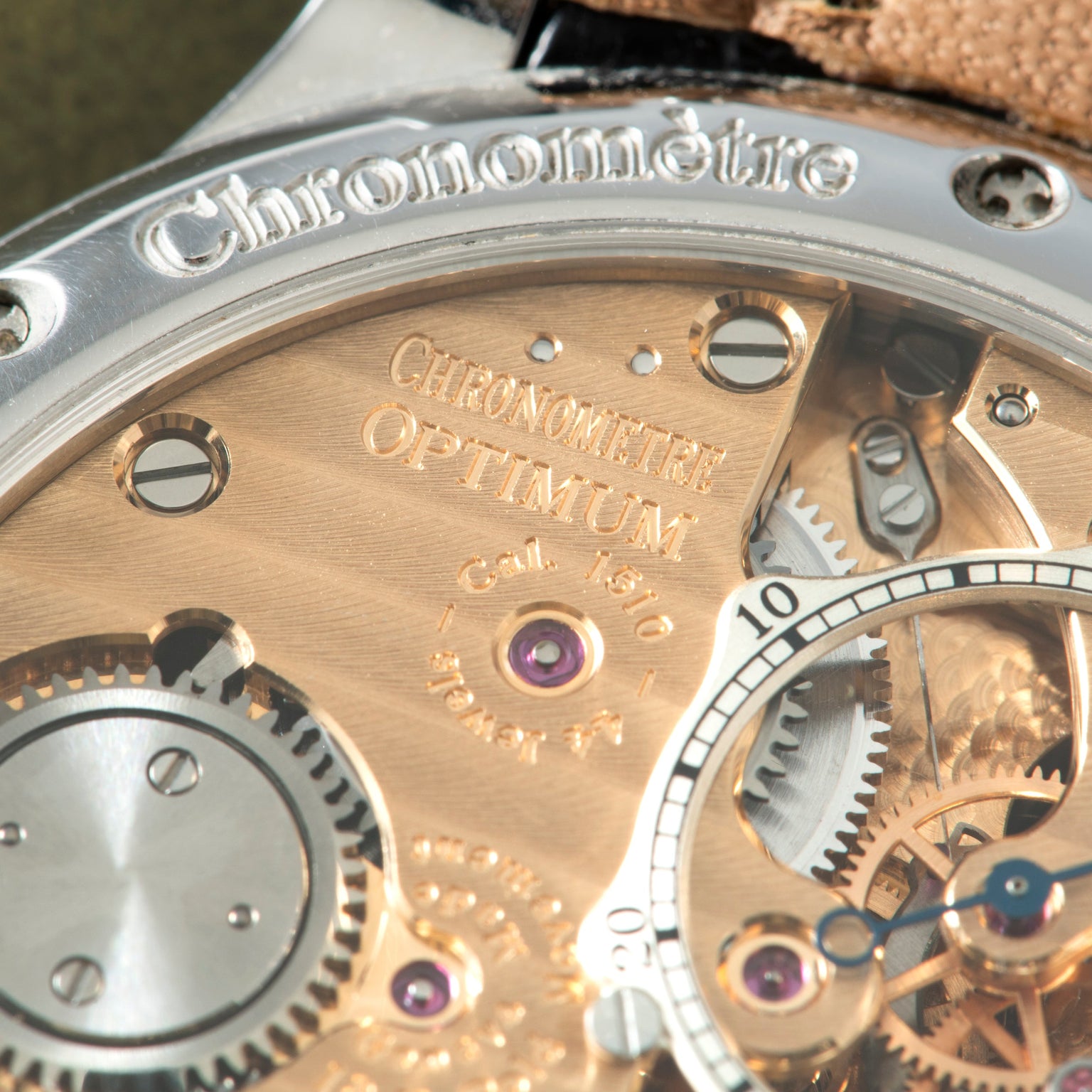 Rose gold watch movement with "Chronomètre Optimum" engraving, exposed gears, and purple jewels.