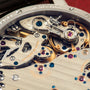 Close-up of watch movement showing polished steel bridge with jumping seconds mechanism and colorful jewels.