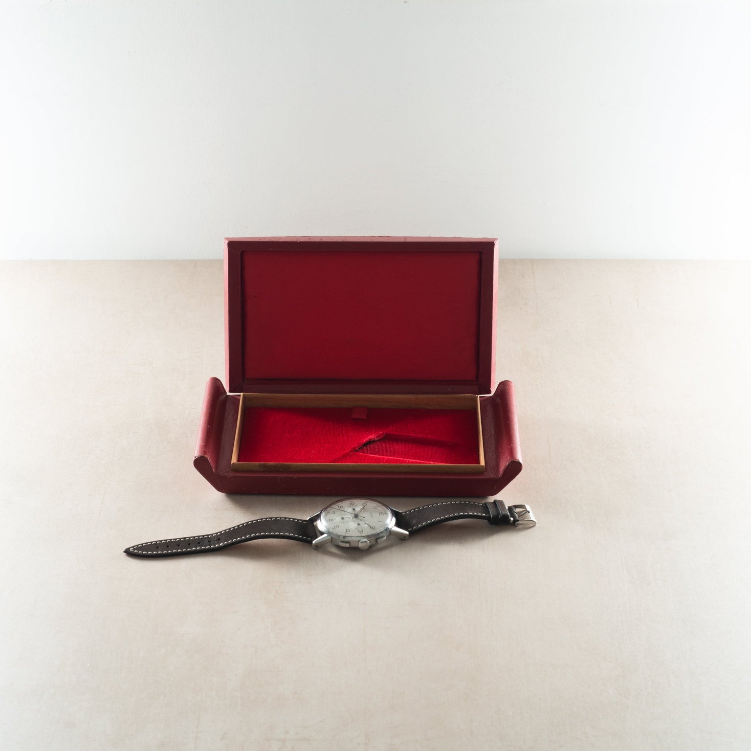 Chronograph watch with silver dial and black leather strap displayed with open burgundy presentation box.