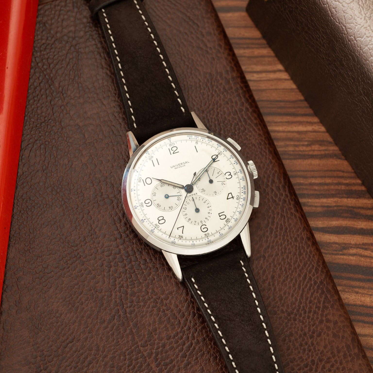 Universal Genève Jumbo Compax chronograph watch with cream dial, black leather strap, and stainless steel case on wood surfac