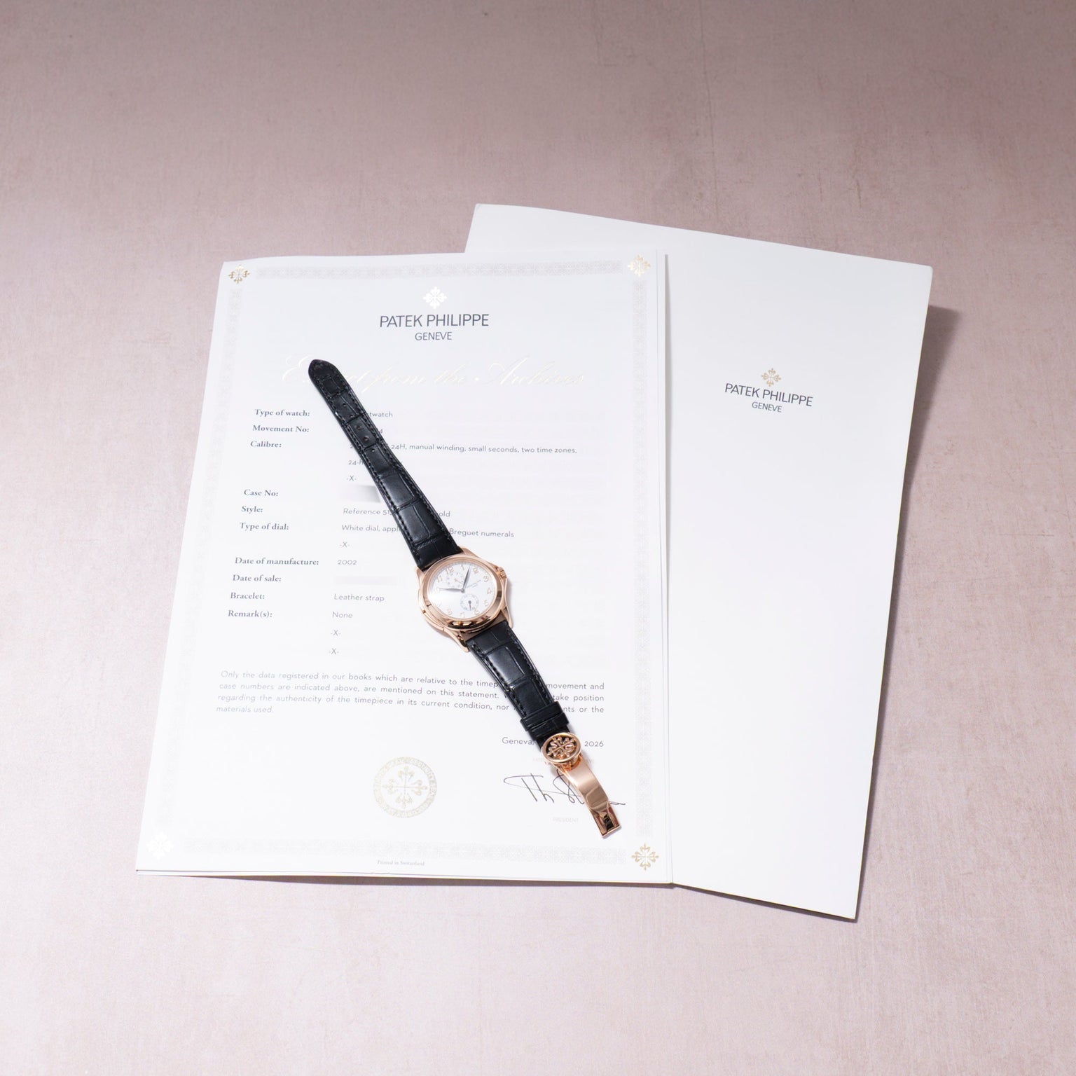 Patek Philippe Calatrava wristwatch with rose gold case, cream dial, and black leather strap displayed on documentation paper