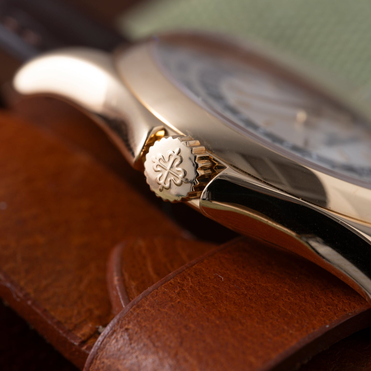 Luxury watch with silver case and brown leather strap, crown detail visible, resting on wooden surface.