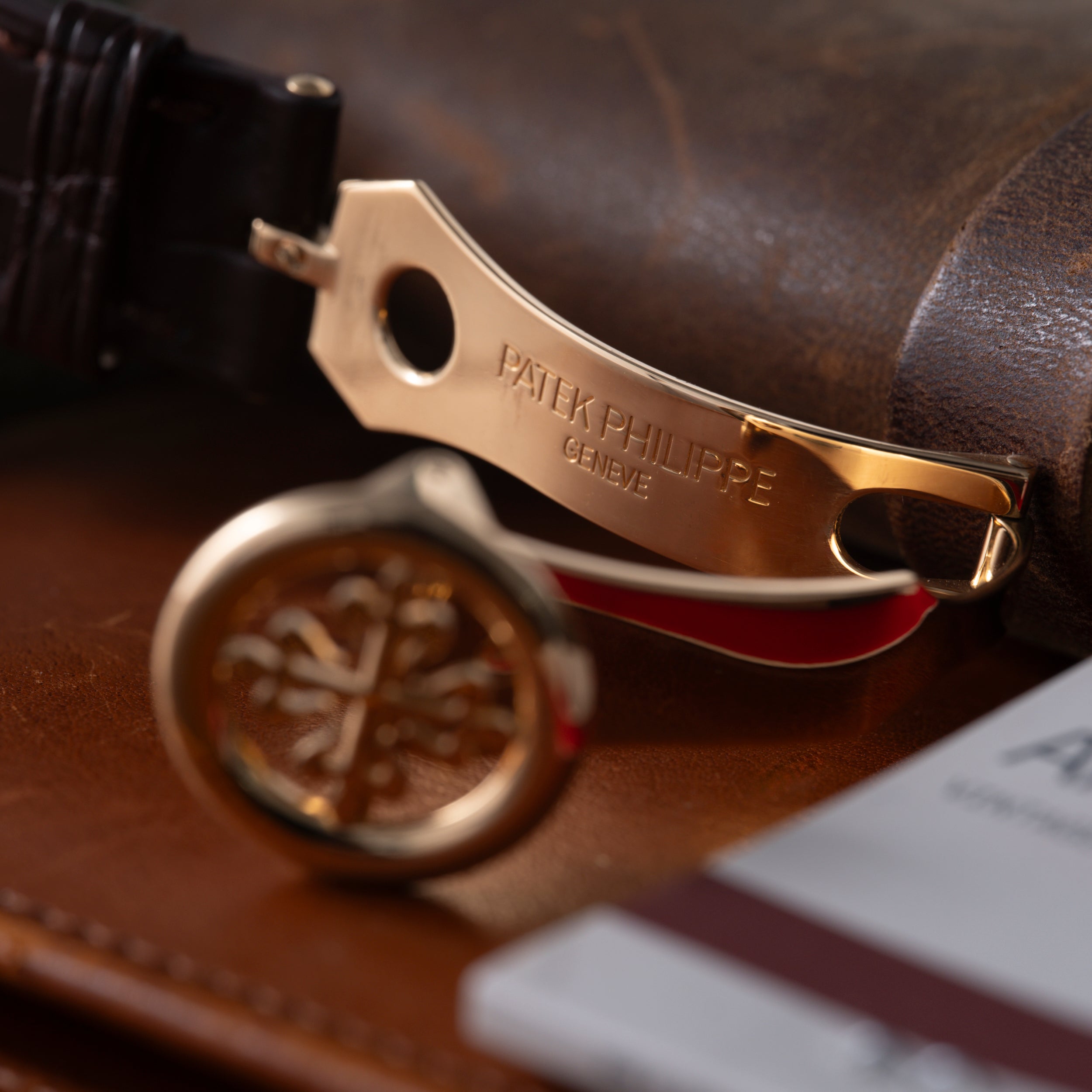 Gold-tone Patek Philippe watch with black leather strap resting on brown leather surface.