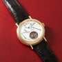 Gold-toned watch with white dial, Roman numerals, visible tourbillon at 6 o'clock, and black crocodile leather strap.