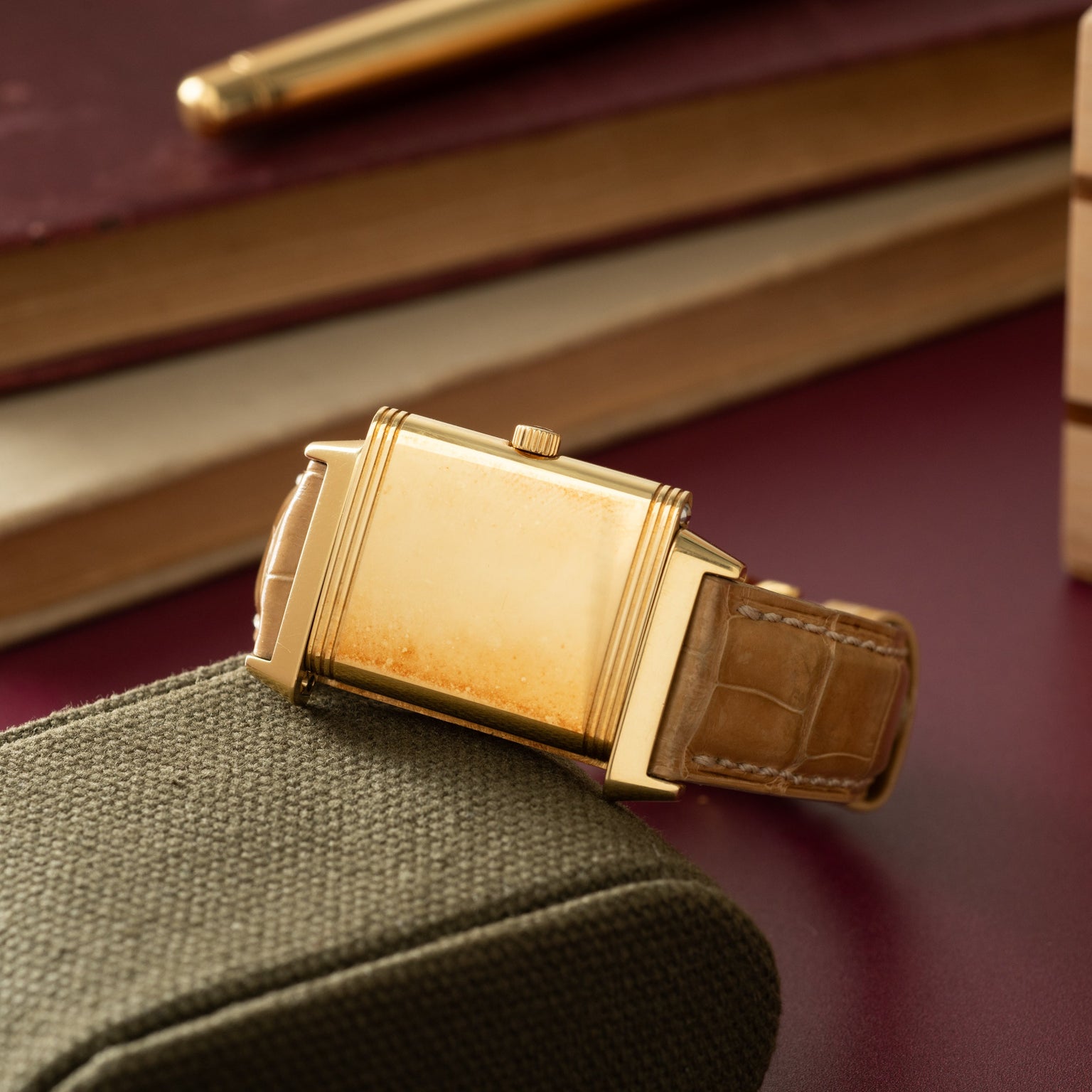 Gold-tone rectangular watch with cream dial and brown leather strap on fabric surface.