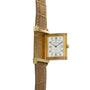 Gold-tone rectangular watch with cream dial, Arabic numerals, and brown leather strap with white stitching.