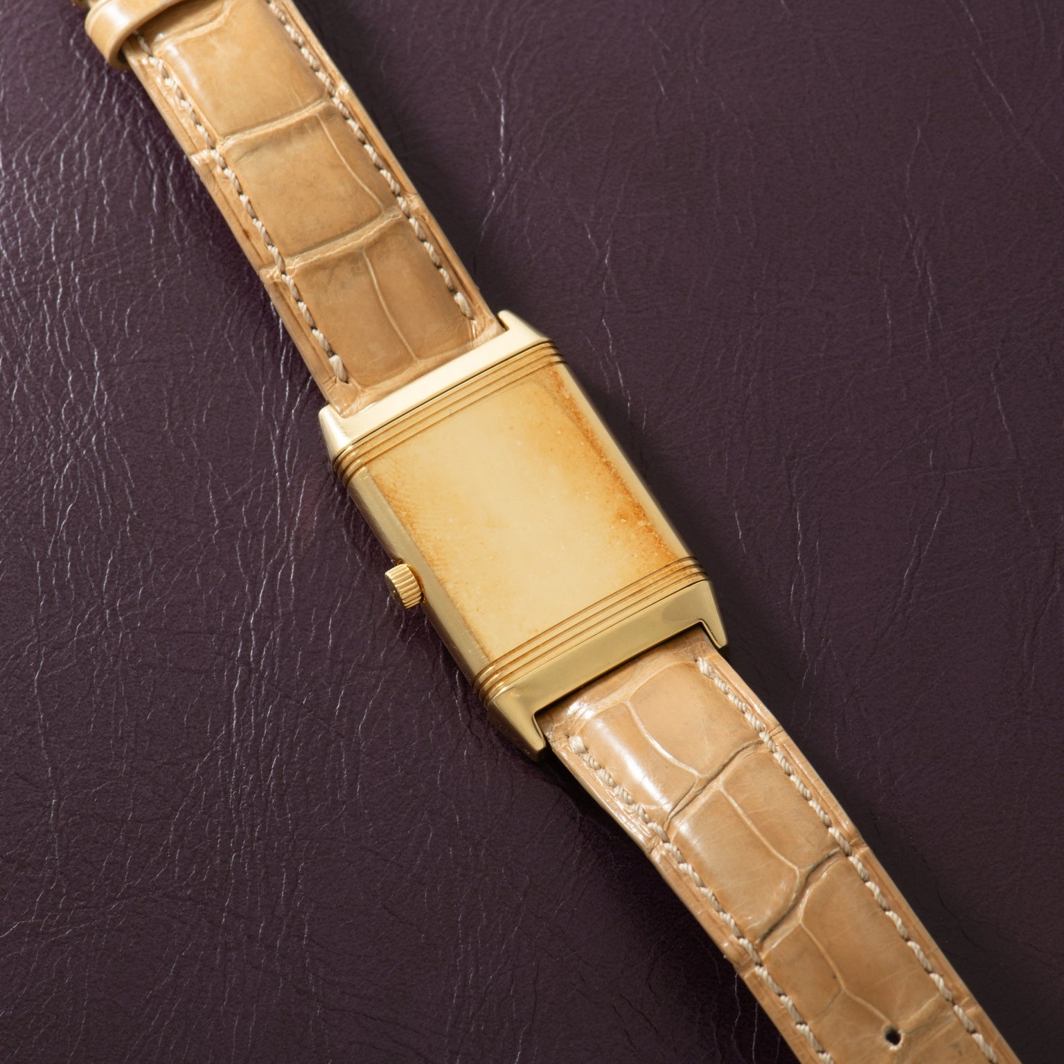 Gold-tone rectangular watch with cream dial and tan crocodile leather strap on dark background.