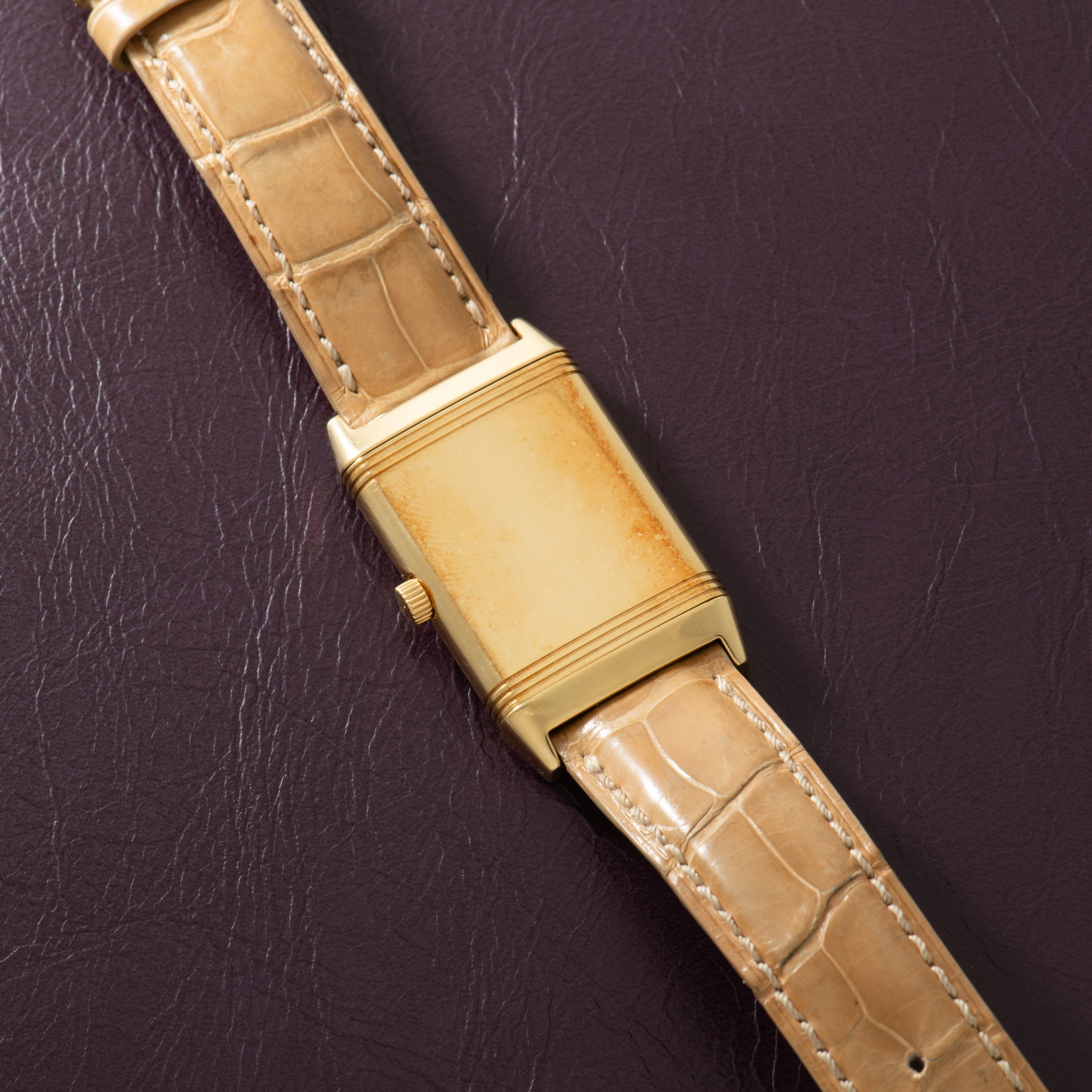 Gold-tone rectangular watch with cream dial and tan crocodile leather strap on dark background.