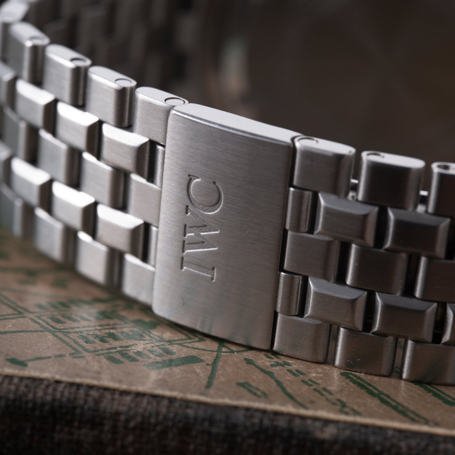 Stainless steel watch bracelet with IWC logo engraved on clasp, angled view showing links and clasp detail.