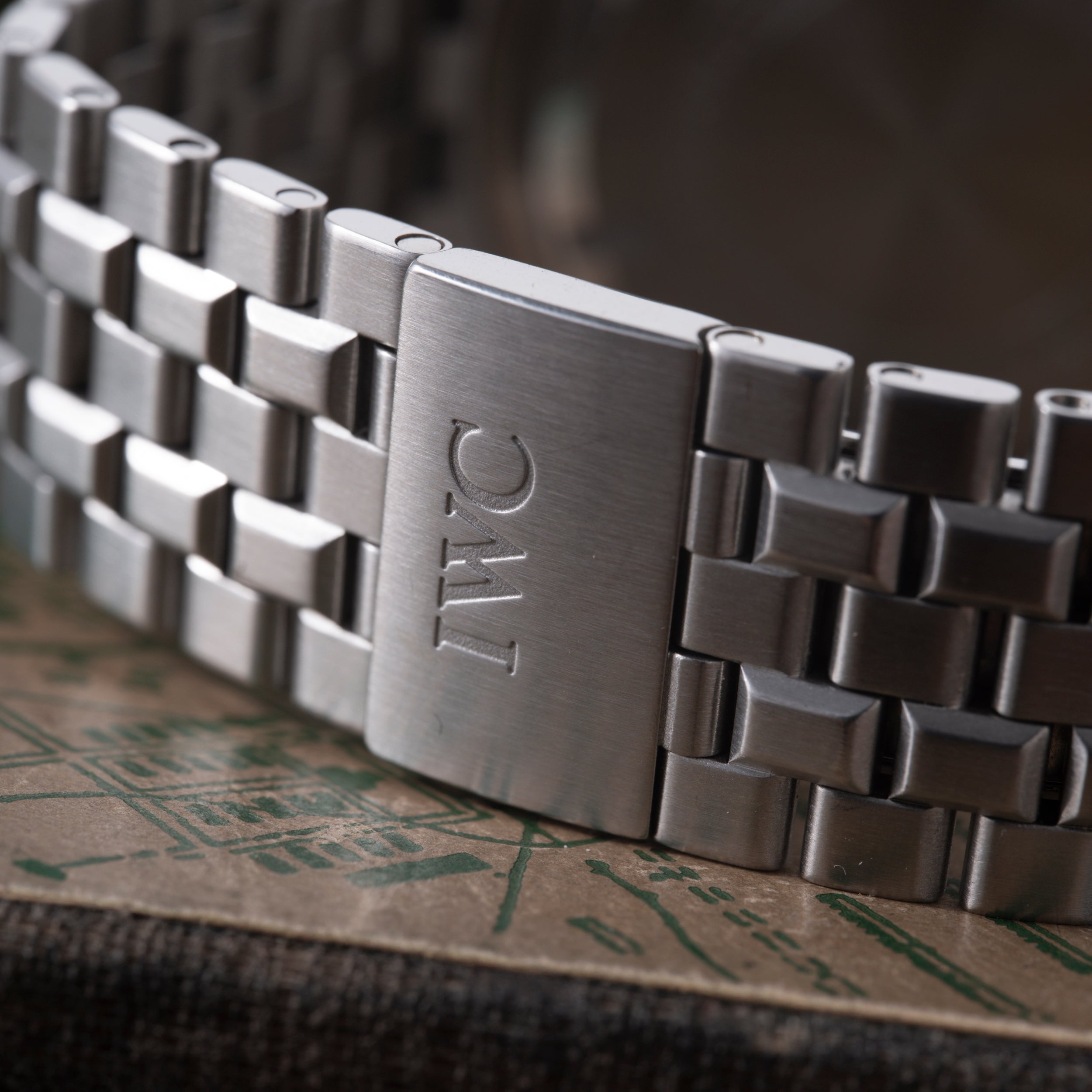 Stainless steel watch bracelet with IWC logo engraved on clasp, angled view showing links and clasp detail.