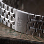 Stainless steel watch bracelet with IWC logo engraved on clasp, angled view showing links and clasp detail.