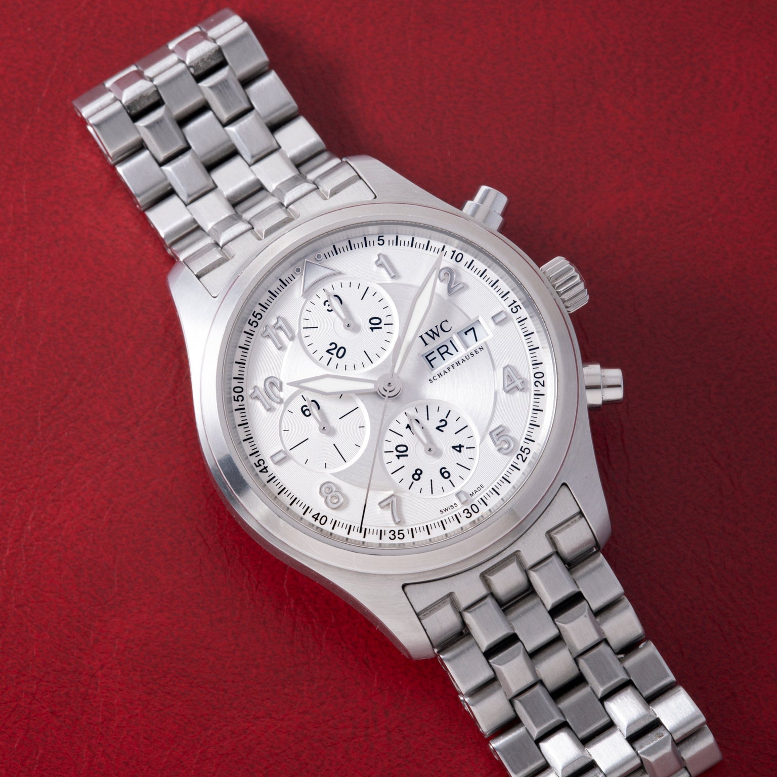 Stainless steel chronograph watch with silver dial, multiple subdials, date window, and matching bracelet on red background.