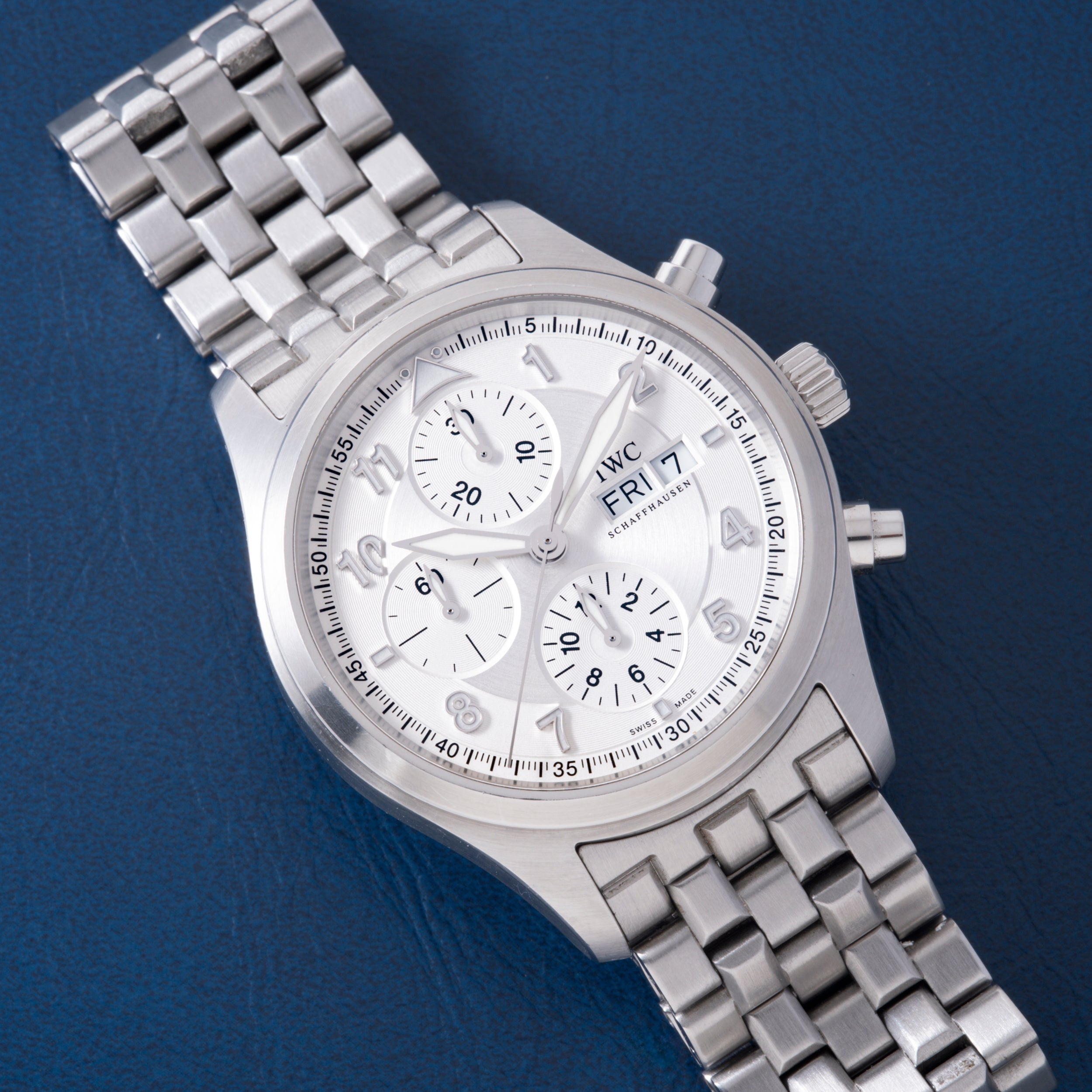Silver-tone chronograph watch with white dial, three subdials, Arabic numerals, and stainless steel bracelet on blue backgrou