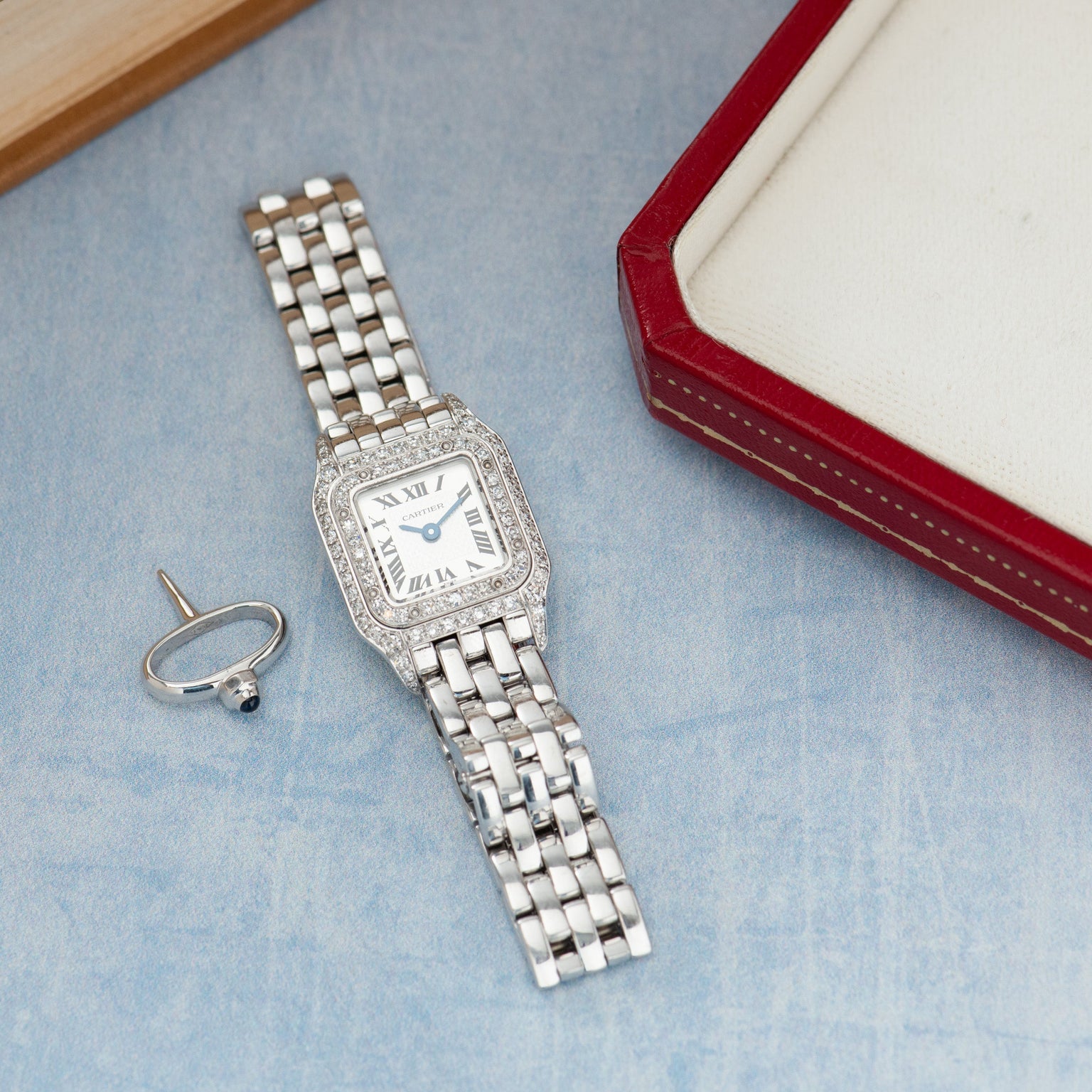 Silver-toned rectangular watch with diamond-set bezel, cream dial with Roman numerals, metal bracelet, displayed with ring an
