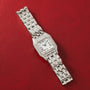 Silver-toned watch with square face, diamond-set bezel, Roman numerals, and matching metal bracelet on red background.
